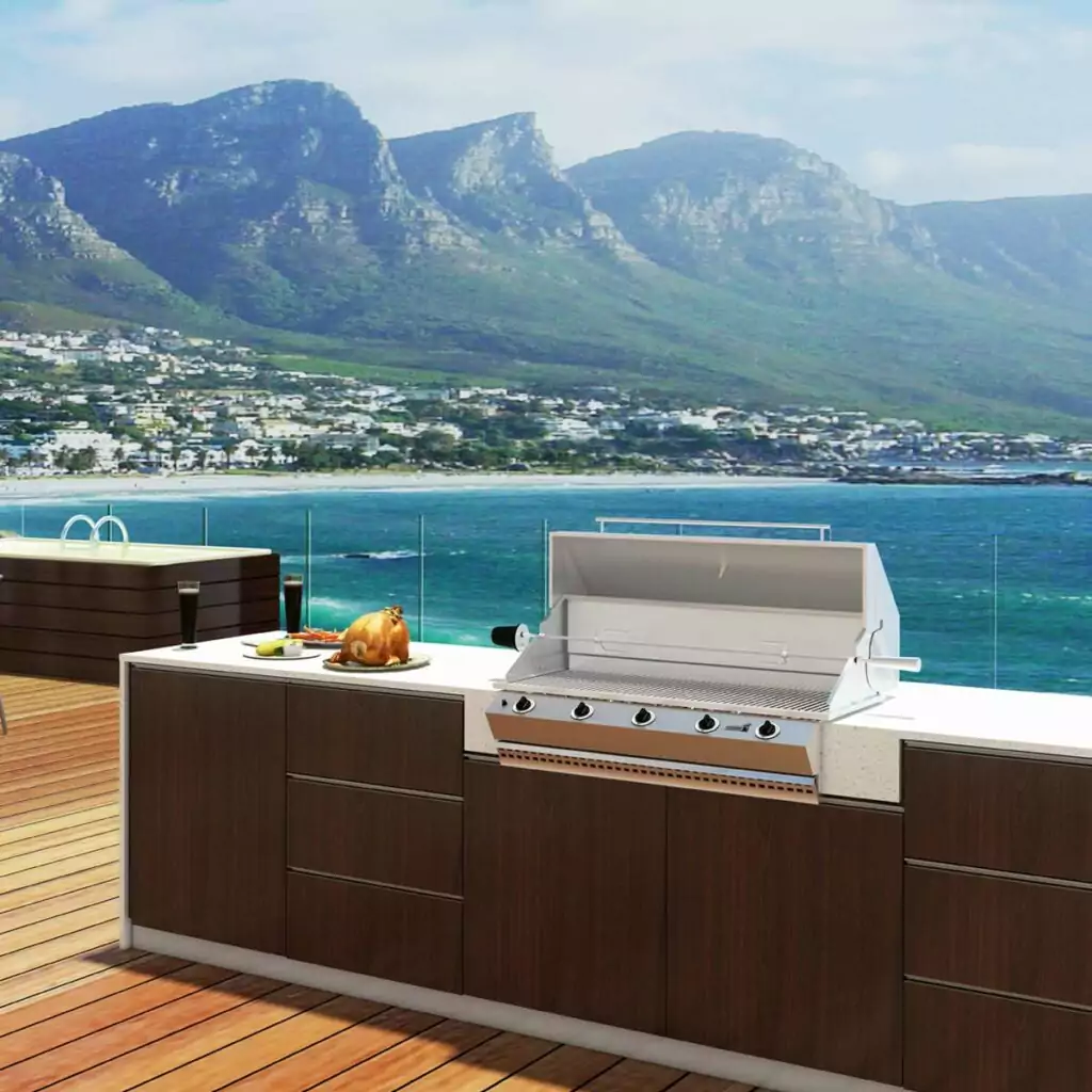 Outdoor deck kitchen with a built-in grill, dark wood cabinets, and a plate of roasted turkey beside the grill, overlooking the sea and distant mountains.